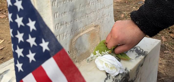 Tending specialist respectfully laying flowers at a veterans monument, demonstrating our philosophy of dignified grave care