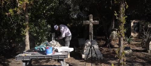 Tending specialist restoring a broken cross-shaped cemetery monument.