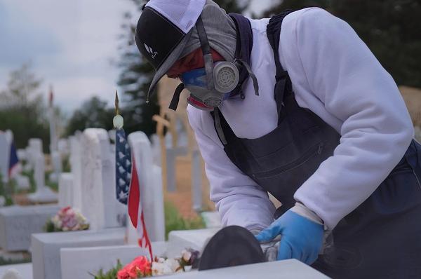 Tending specialist performing gentle headstone cleaning and grave maintenance.