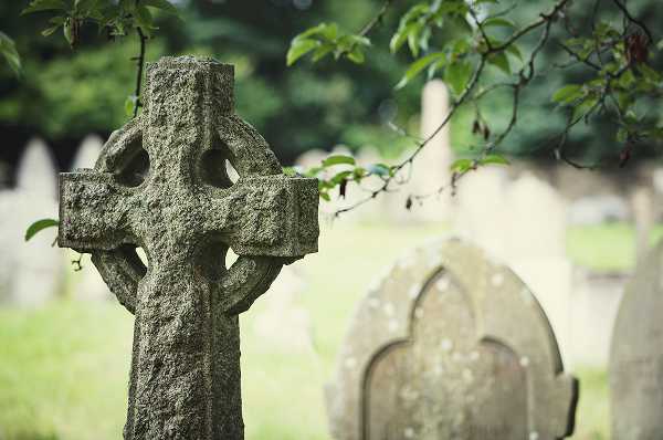 Aged Celtic cross monument at a cemetery showing natural stone weathering