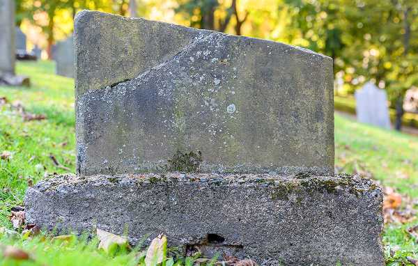 A chipped cemetery tombstone heavily covered in green moss and biological growth