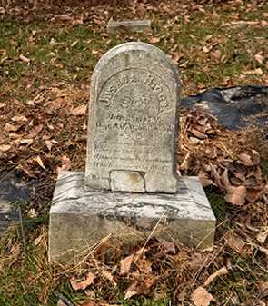 A severely leaning and dirty granite monument suffering from frost heave damage