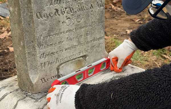 Tending specialist using precise leveling tools to reset an upright cemetery monument