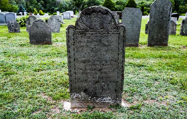 A heavily weathered gravestone with a barely discernible inscription due to biological growth and time