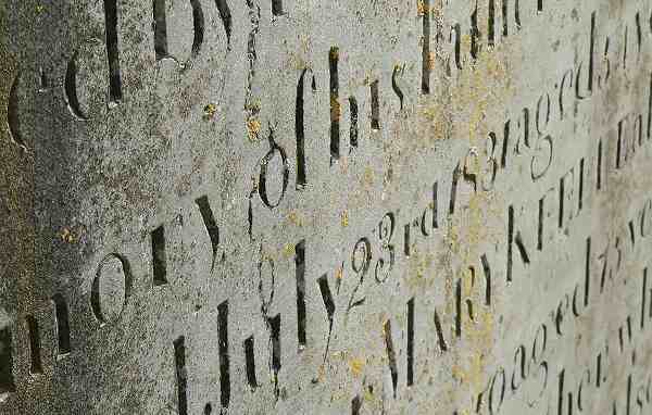 Close-up of a weathered ancient tombstone showing a severely faded and barely noticeable carved inscription.