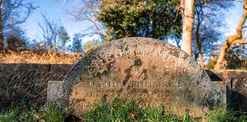 A heavily eroded semicircular gravestone with faded inscriptions, highlighting the need for professional headstone letter restoration.