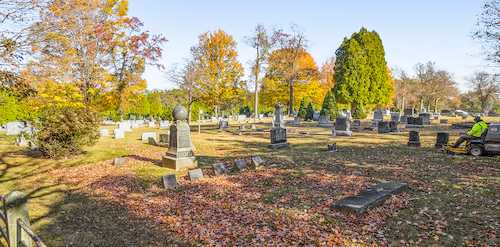 Cemetery worker clearing fallen leaves from headstones in autumn