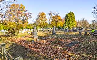 Cemetery worker clearing fallen leaves from headstones