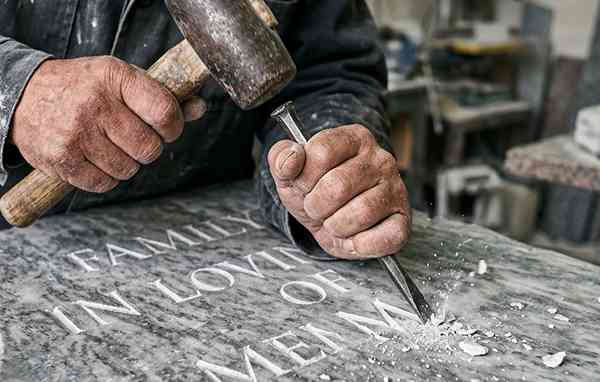 Stonemason hand-carving an inscription into a headstone with a hammer and chisel