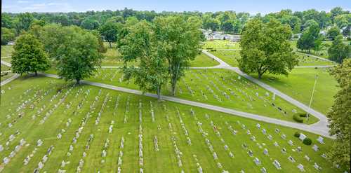 Aerial view of a cemetery in summer with rows of headstones, lawns, and roads