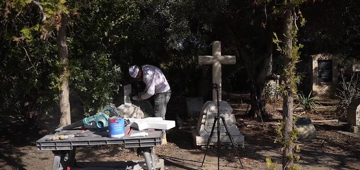 Tending specialist performing a step-by-step restoration of a cross-shaped monument, demonstrating our safe and professional grave care process